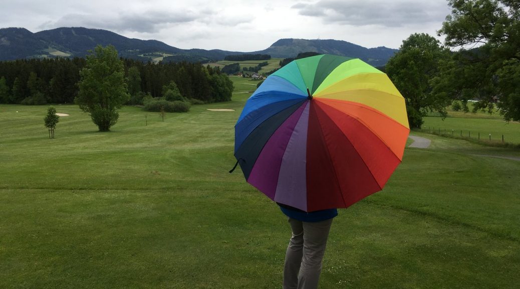 Golferin mit Regenbogenschirm am Golfplatz